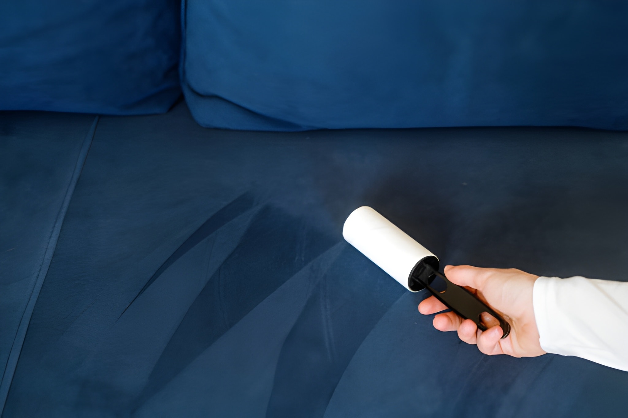 Closeup on woman hand remove dust and hair from couch upholstery using roller lint.